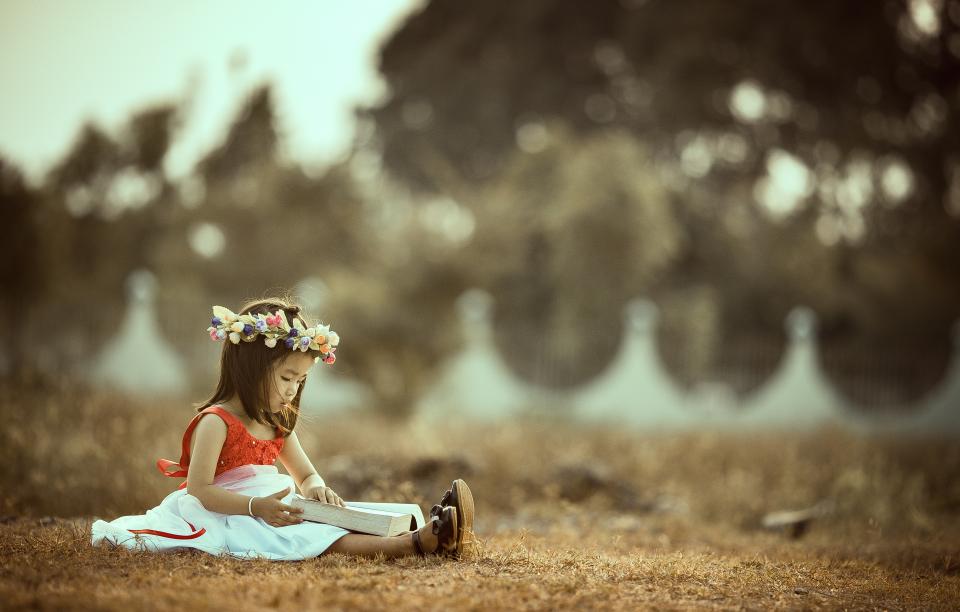 Une enfant plongée dans son livre, installée dans l'herbe