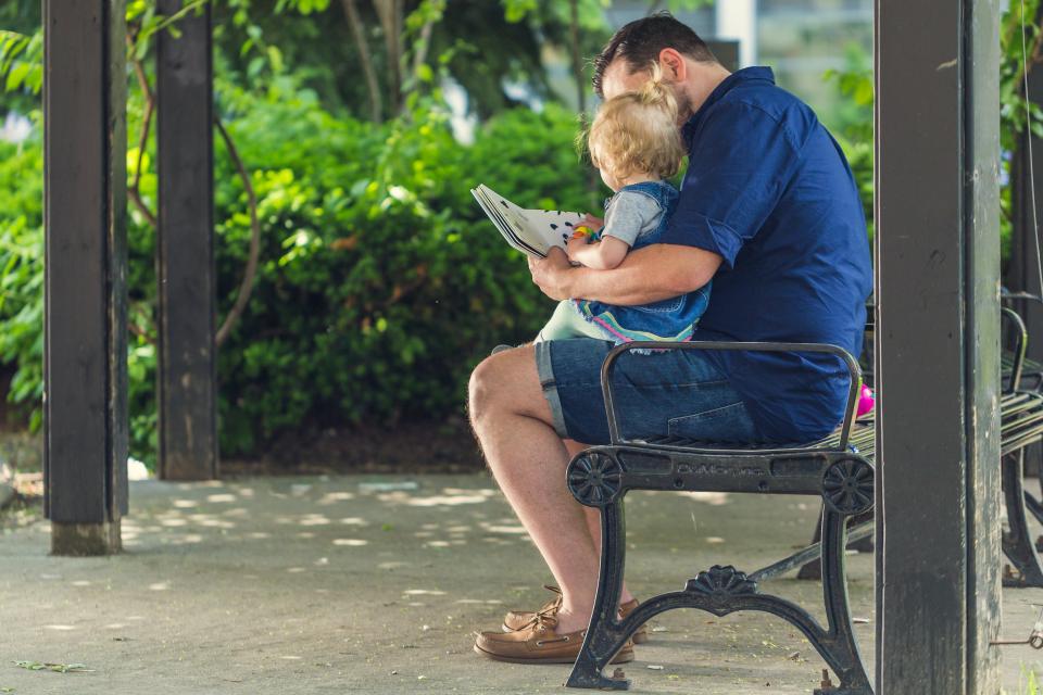 Un père lit un album avec sa fille, assis sur un banc